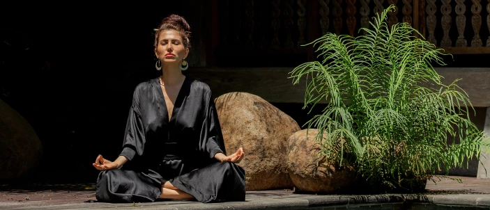 Woman meditating outdoors beside tropical plants